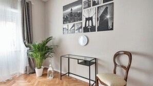 Une pièce dotée d’un parquet en bois disposé en motif « chevron », d’une table en verre, d’une chaise en bois, d’une plante en pot et d’un mur orné de photographies en noir et blanc représentant des paysages urbains.