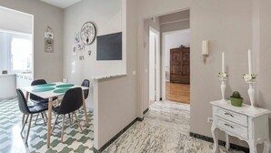 Un coin repas avec une table et des chaises, une horloge au mur et un couloir menant à une autre pièce.
