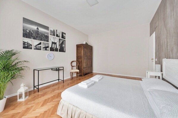 Een slaapkamer met een bed, een bureau, een stoel, een kledingkast en een potplant.