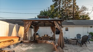 A hot tub with a canopy, surrounded by outdoor furniture and a stone fire pit.