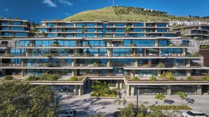 A multi-story hotel with a modern design, featuring balconies, outdoor seating areas, and a view of a hill with residential buildings in the background. - RJS Savoy Monumentalis (Funchal)
