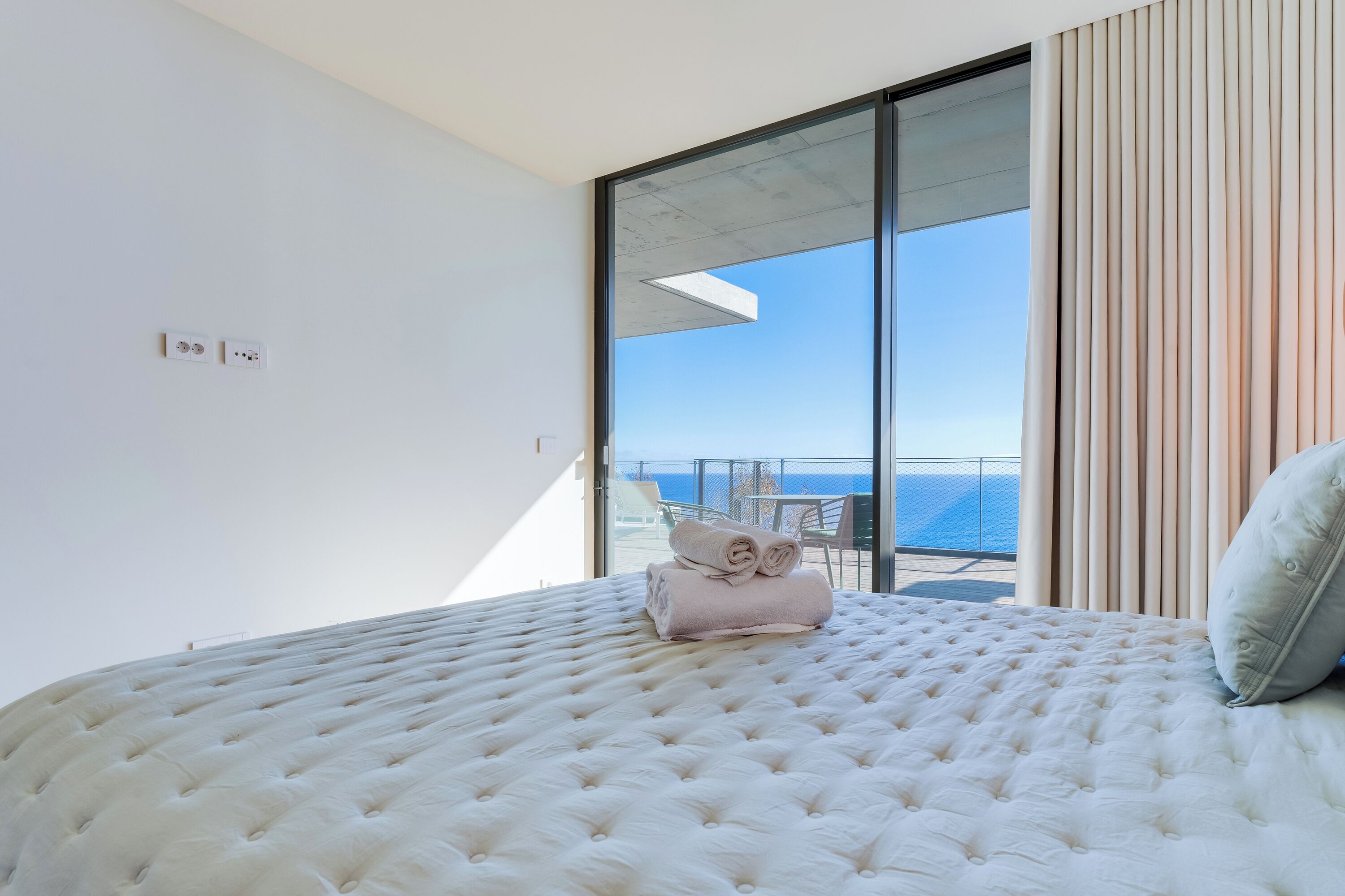 A bedroom with a large bed, a view of the sea, and a balcony with a table and chairs.