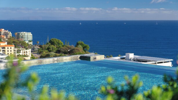 A clear blue swimming pool with a view of the ocean and buildings in the background. - RJS Savoy Monumentalis (Funchal)