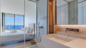 A modern bedroom with a large bed, a glass shower enclosure, and a view of the sea. - RJS Savoy Monumentalis (Funchal)