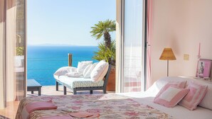 Un dormitorio con cama, una silla, una lámpara y vista al mar.