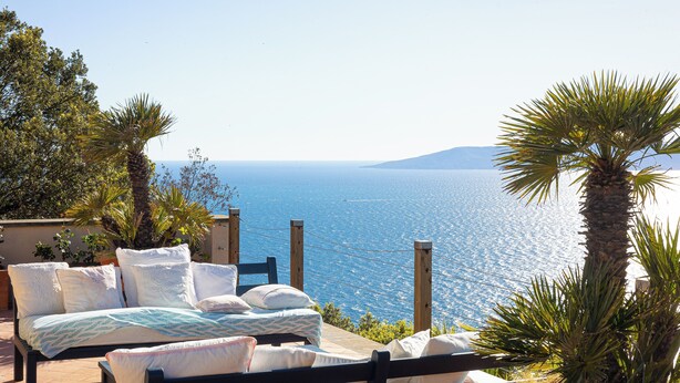 Una cama con sábanas blancas y vista al mar.