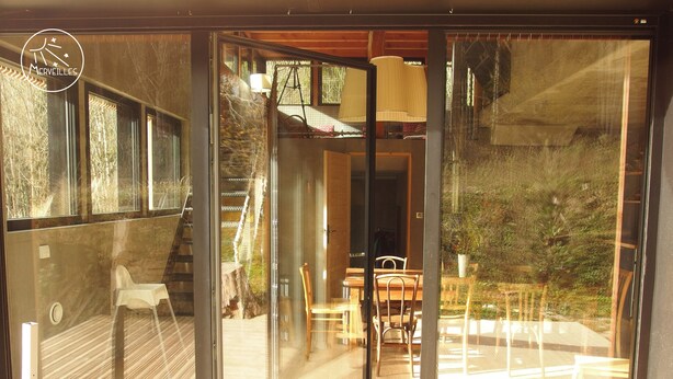 A modern glass door leading to an outdoor deck with a wooden table and chairs, a staircase, and a view of the surrounding greenery. - Self-catering ecogîte in the heart of the forest at La Chapelle-en-Vercors (La Chapelle-en-Vercors)