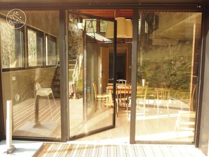 Una porta in vetro moderna che dà su una terrazza esterna con tavolo e sedie in legno, una scala e vista sul verde circostante.
