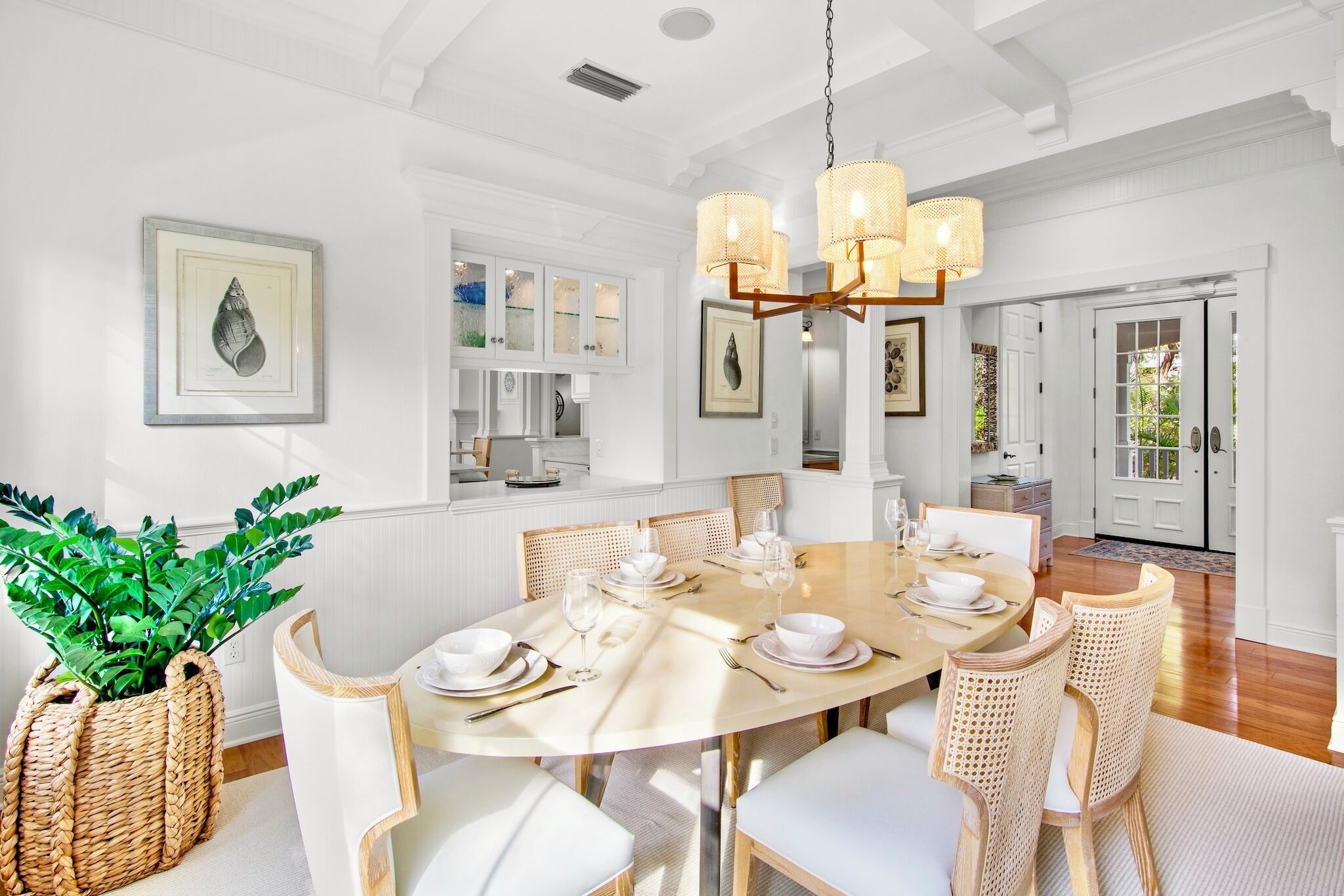 A dining area with a round table set for six, surrounded by wicker chairs, and a chandelier above.