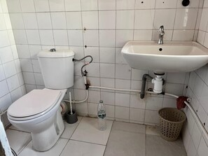 A compact bathroom with a toilet, sink, and laundry basket.