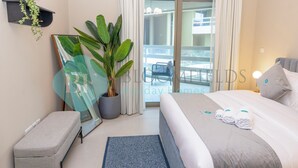 A hotel room with a bed, a bench, a potted plant, a mirror, and a view of the balcony. - Bloomfields Superior1BR Ajwan Soul Beach (Abu Dhabi)