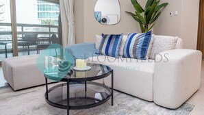 A modern living room with a glass coffee table, a beige sofa with striped pillows, a large mirror, and a potted plant. - Bloomfields Superior1BR Ajwan Soul Beach (Abu Dhabi)