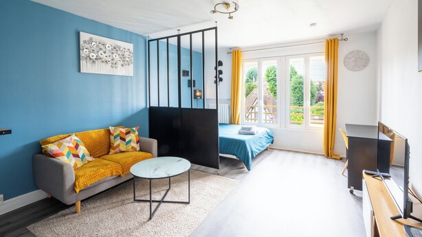 A modern living room with a sofa, coffee table, and a desk with a computer. - Le studio epure du commandant (Évreux)