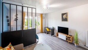 A modern living room with a sofa, a coffee table, a TV, a desk, and a potted plant. - Le studio epure du commandant (Évreux)