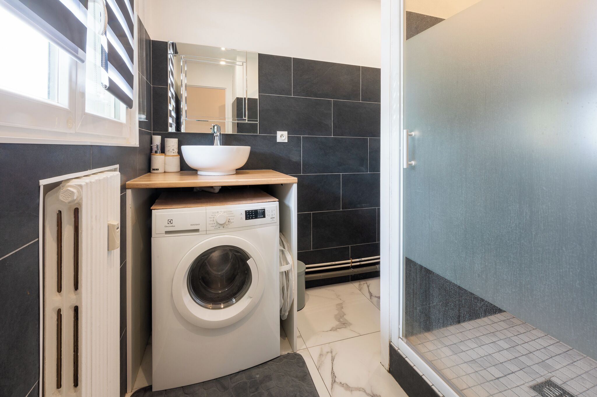 Een kleine badkamer met een wasmachine, een wastafel en een douche.