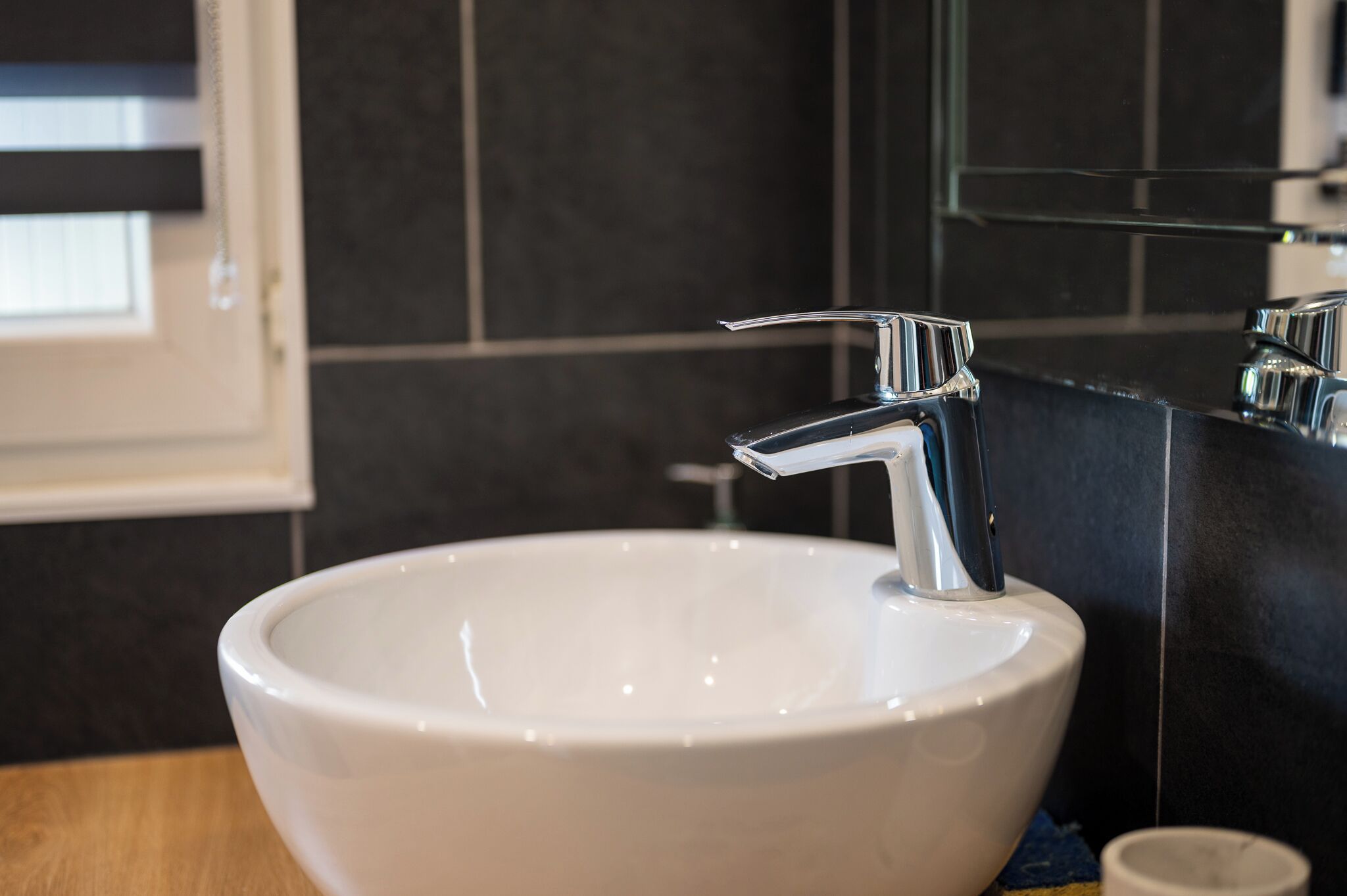 Un lavandino in ceramica bianca con un moderno rubinetto cromato in un bagno con pareti piastrellate scure.
