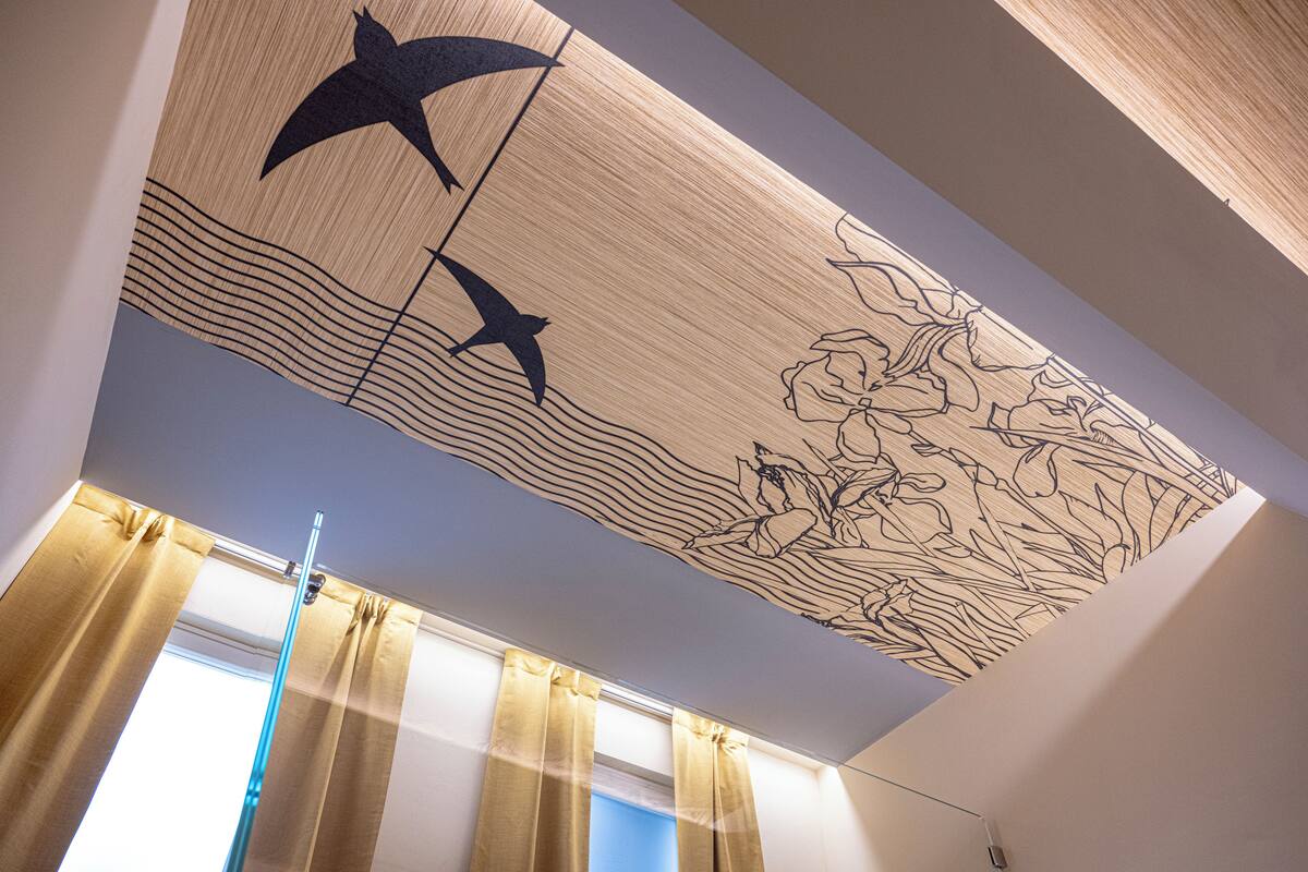 A room with a ceiling mural depicting birds and flowers, a window with curtains, and a visible light fixture.