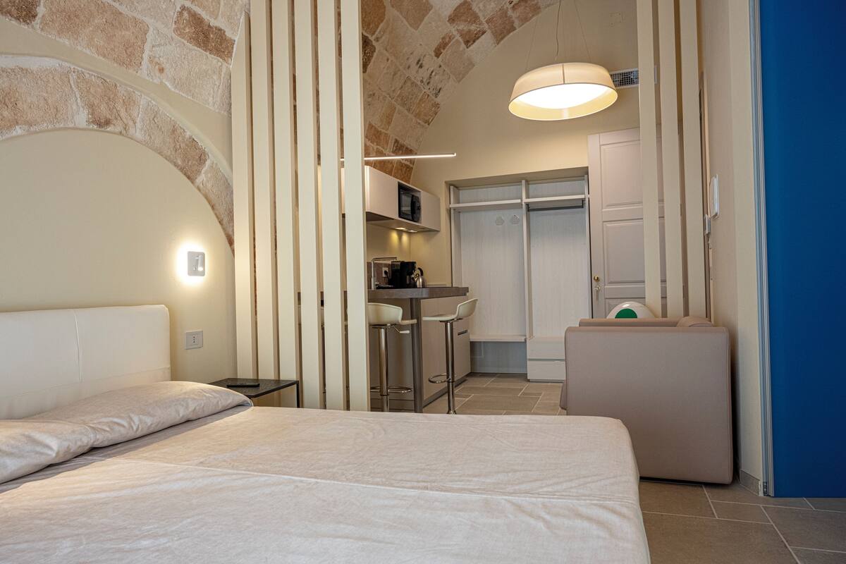 A modern hotel room with a bed, a small kitchenette, and a bathroom.