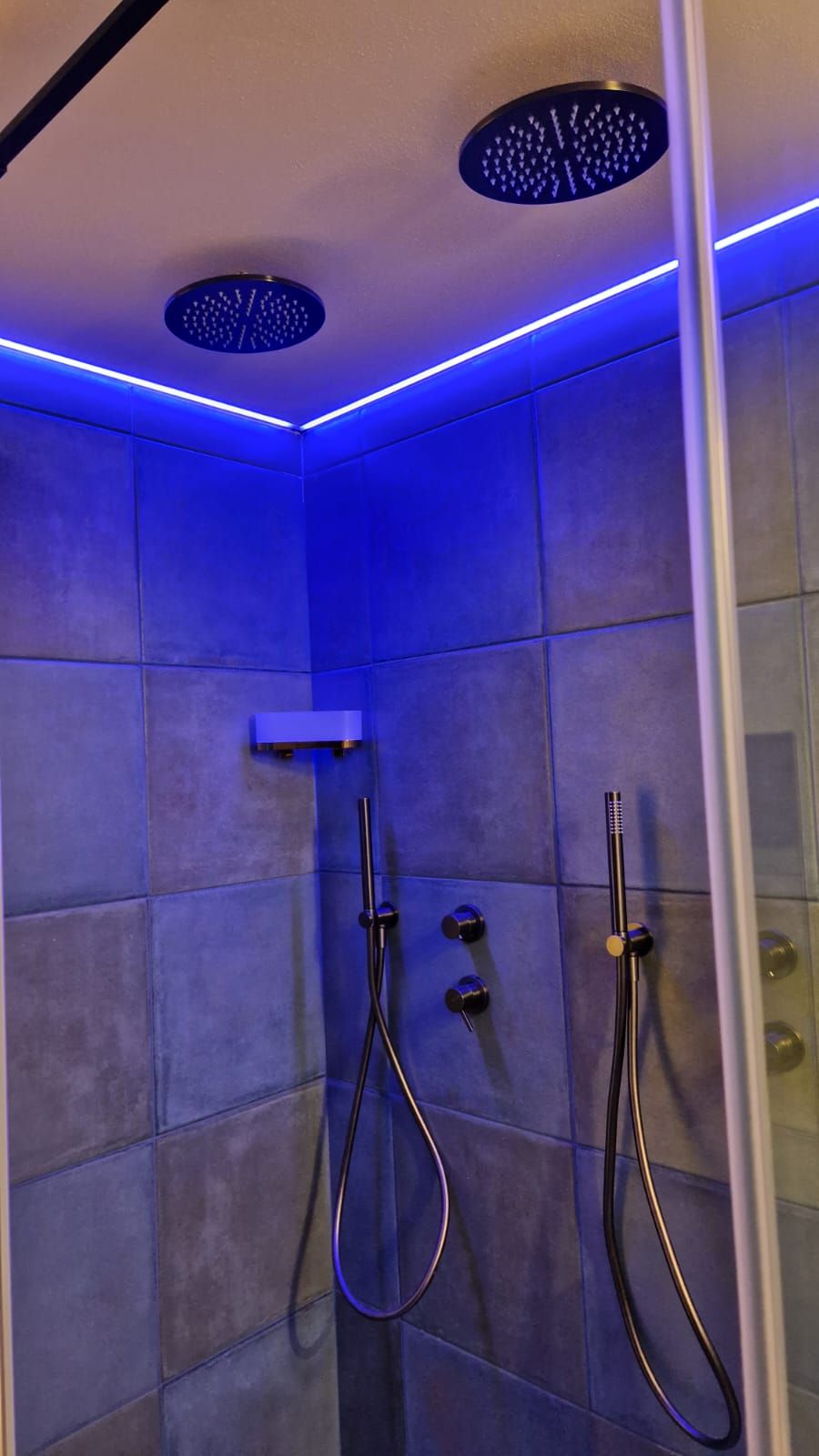 A modern shower with blue LED lighting, a handheld showerhead, and a wall-mounted faucet.