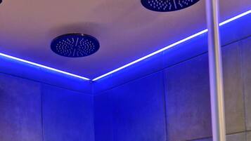 A modern shower with blue LED lighting, a handheld showerhead, and a wall-mounted faucet.
