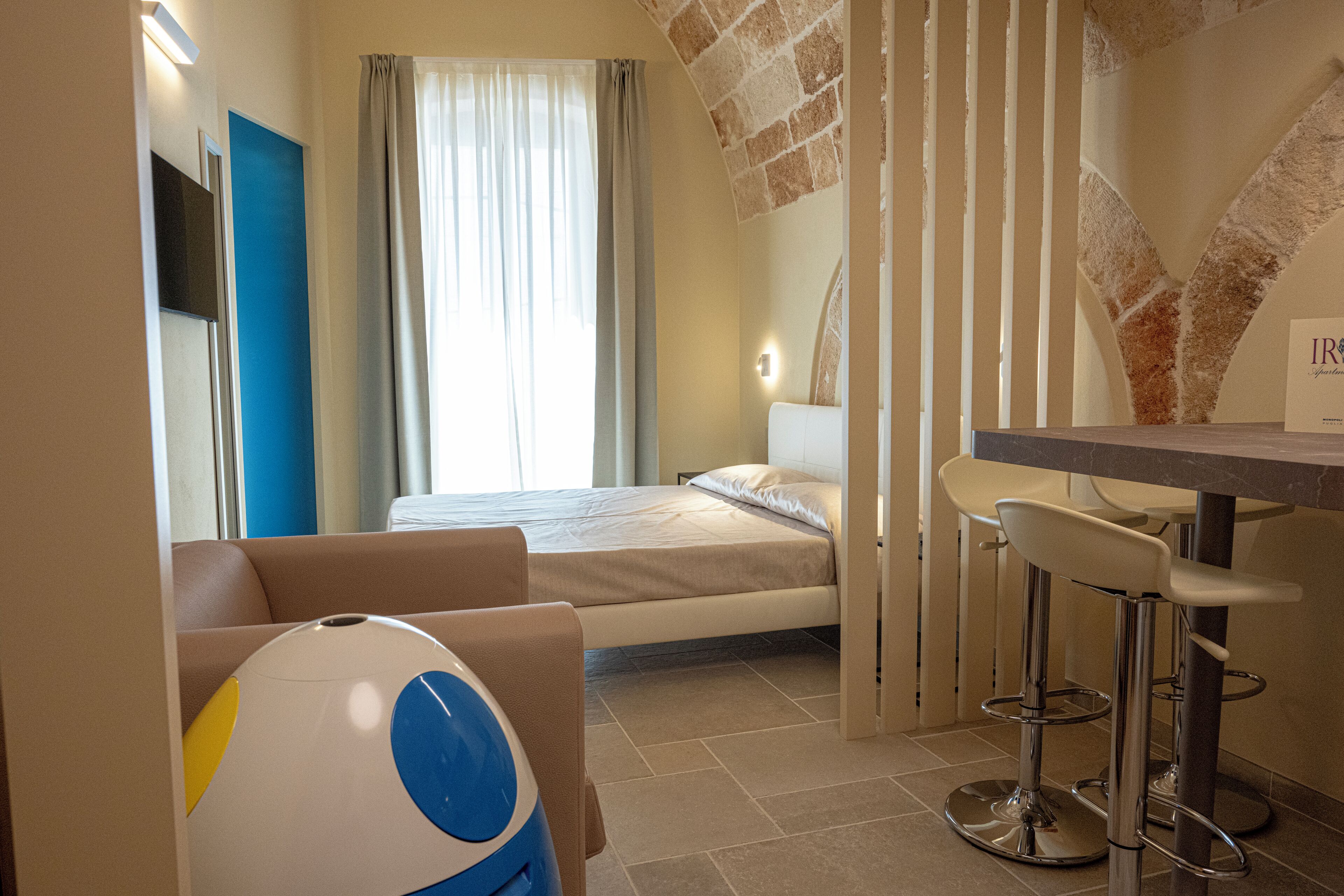 A hotel room with a bed, a desk with two chairs, a large mirror, and a window with curtains.