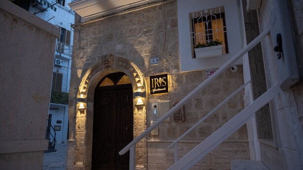 A stone building with a dark wooden door, a sign reading "IRIS", and a staircase leading up. - Iris Apartments (Monopoli)