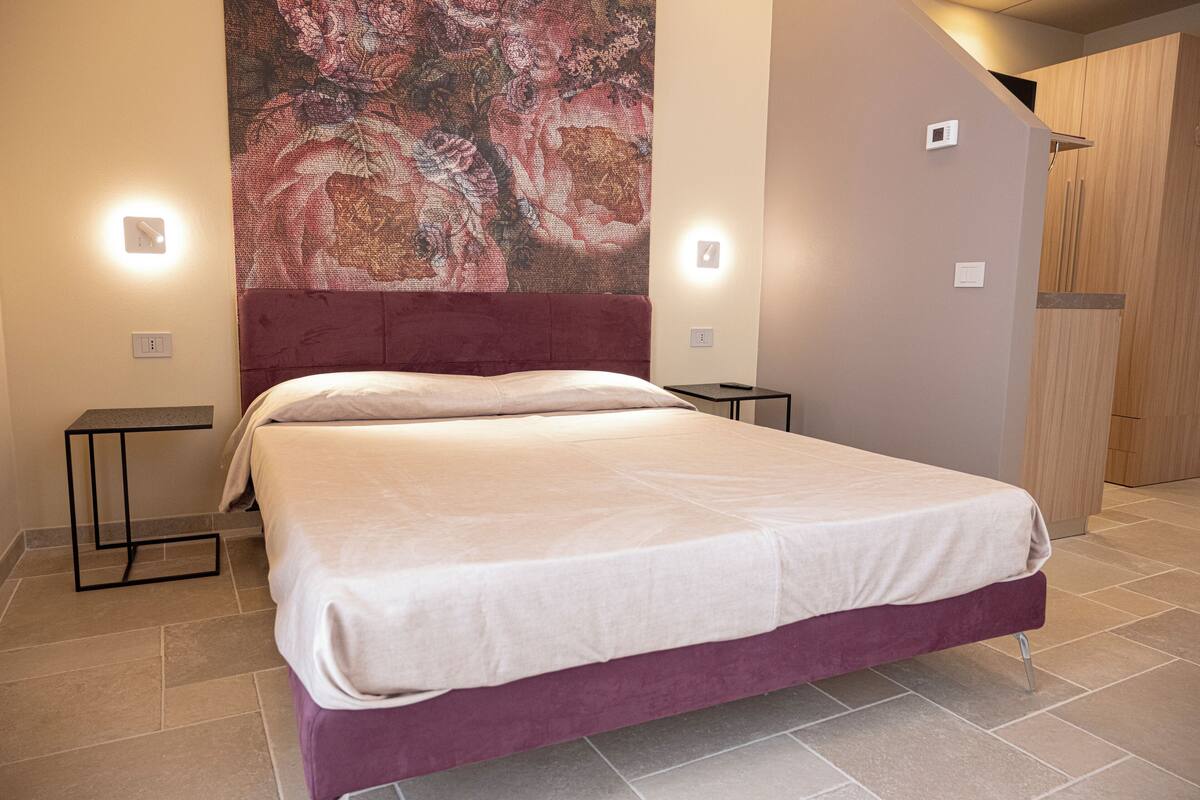 A modern bedroom with a large bed, a headboard, bedside tables, and a wall-mounted light fixture.