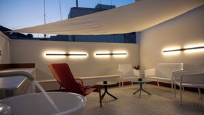 A modern outdoor seating area with white and red chairs, a small round table, and a large white bucket. - Iris Apartments (Monopoli)
