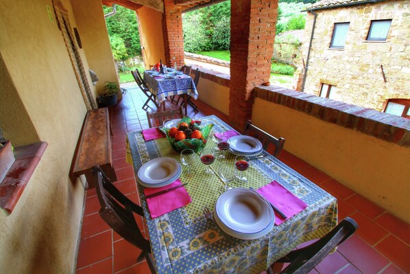 An outdoor dining area with a table set for four, surrounded by brick walls and a view of greenery. - Cottage in Tuscany With Patio (Castiglione d'Orcia)