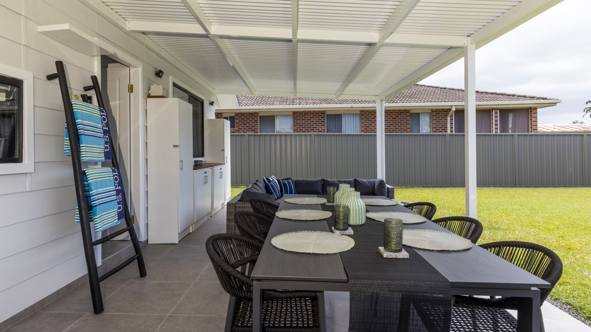 A covered outdoor dining area with a long table, black wicker chairs, and a white ceiling.
