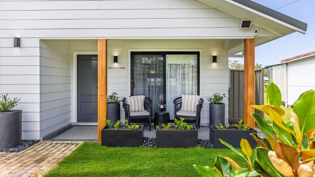 Een modern huis met een overdekte veranda, twee rieten stoelen en potplanten.