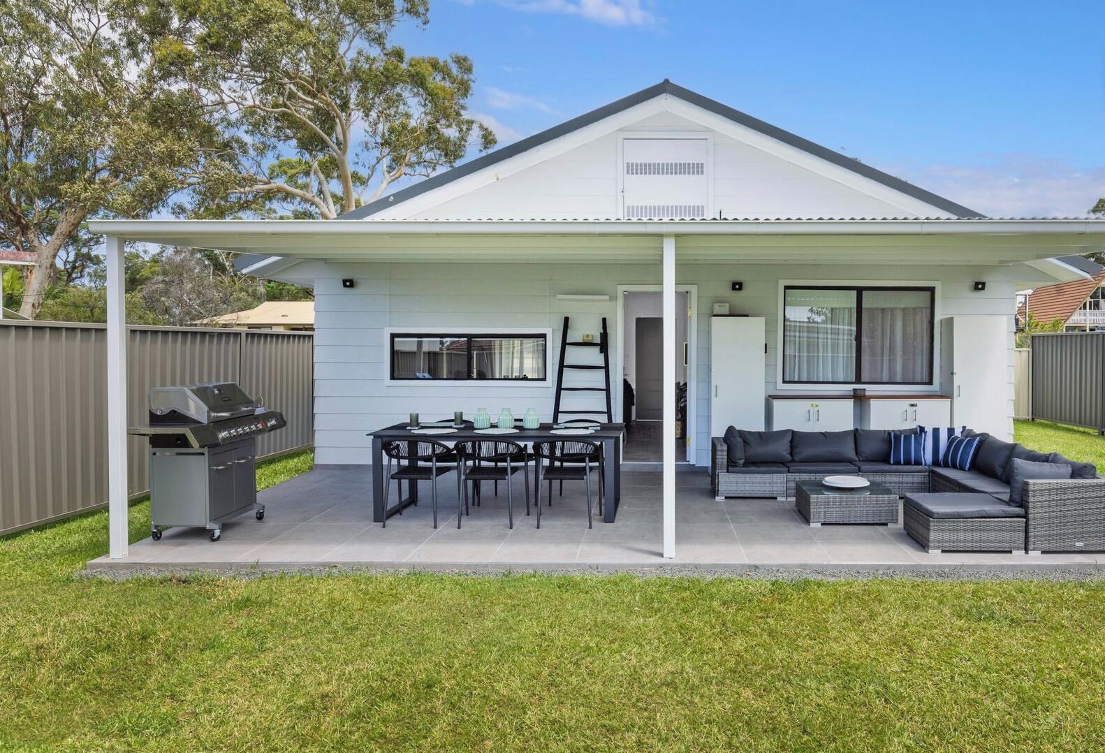 Une maison moderne dotée d’un patio couvert, d’un barbecue et d’un espace détente avec un canapé et une table.