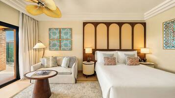 A hotel room with a bed, a sofa, a coffee table, a floor lamp, a wall-mounted fan, and artwork.