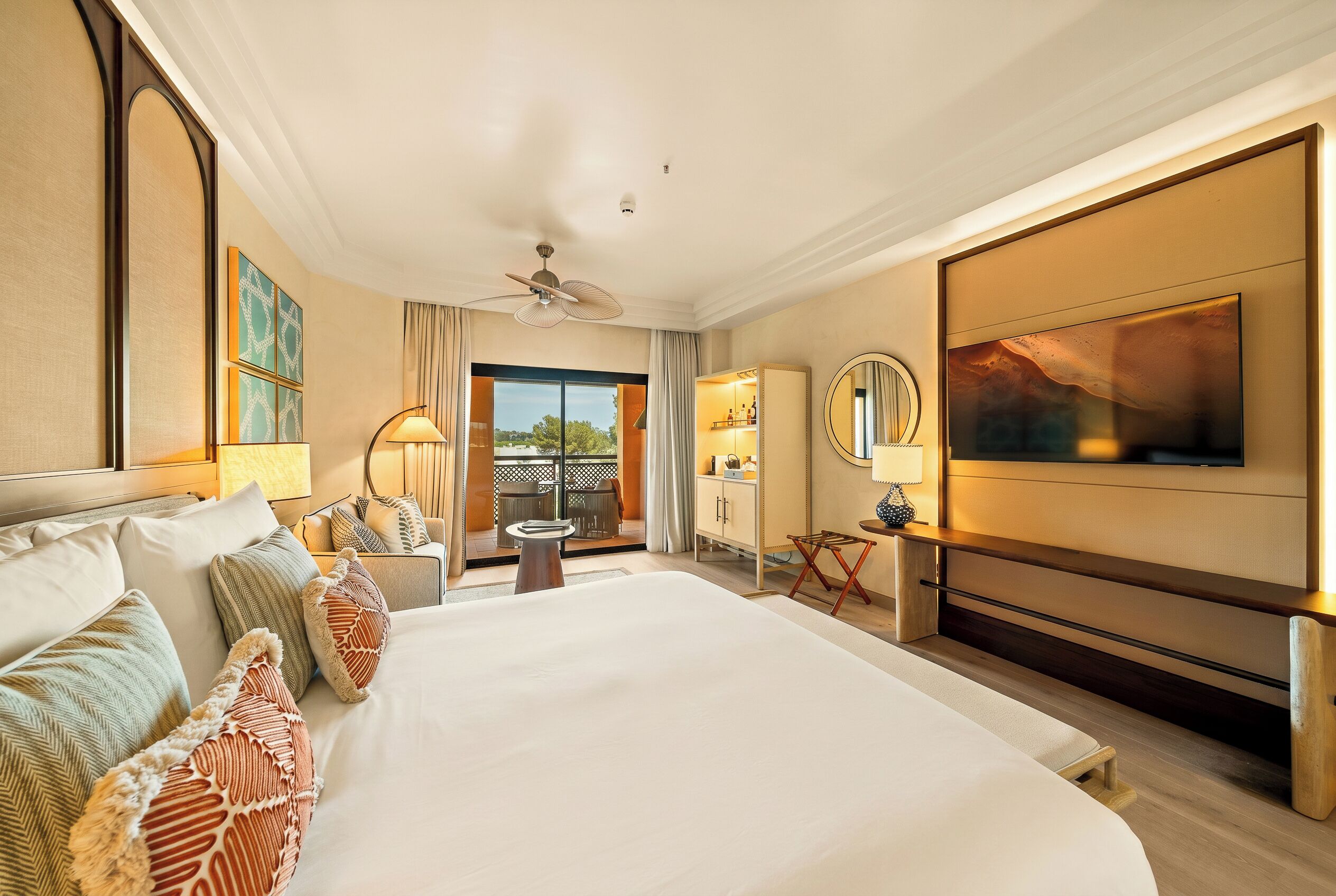 A hotel room with a large bed, a TV, a ceiling fan, and a view of the outdoors.