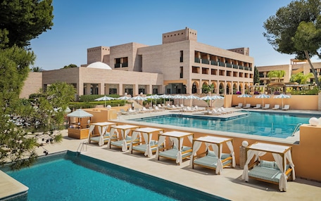 A hotel pool area with sun loungers and umbrellas, surrounded by a building with multiple balconies.