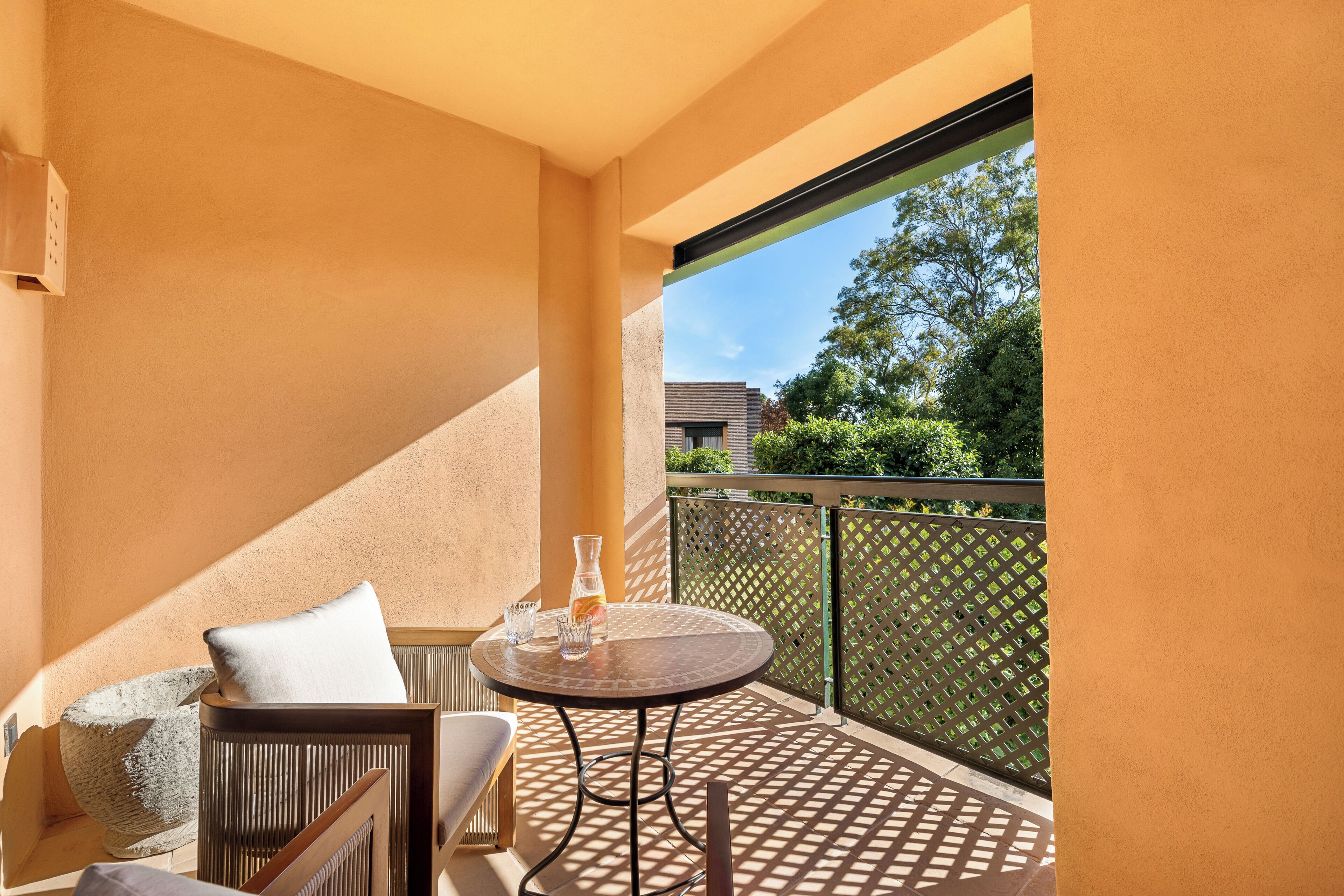 Een balkon met een ronde tafel, twee stoelen, een kussen en een vaas.