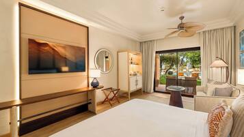 A hotel room with a bed, a TV, a desk, a chair, a sofa, a ceiling fan, and a view of the outdoors.