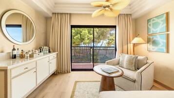Een hotelkamer met balkon, een ronde spiegel, een bank, een salontafel en een plafondventilator.