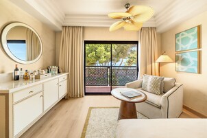 Een hotelkamer met balkon, een ronde spiegel, een bank, een salontafel en een plafondventilator.