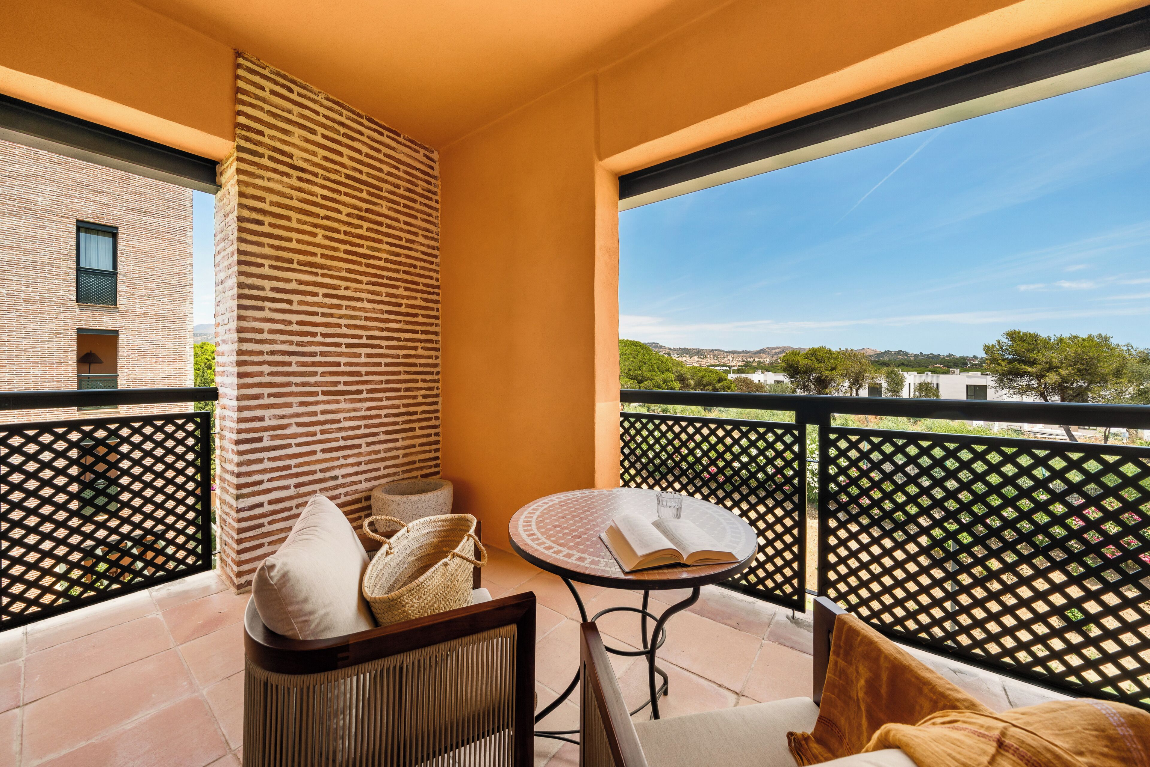 A balcony with a round table, a wicker chair, and a view of a cityscape.