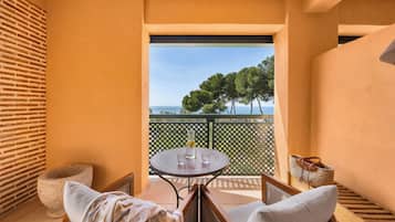 A balcony with a table, chairs, and a view of trees and the sea.