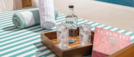 A poolside setting with a striped towel, a bottle of Gran Reserva, two glasses with ice, and a book titled 'ICONIC'.