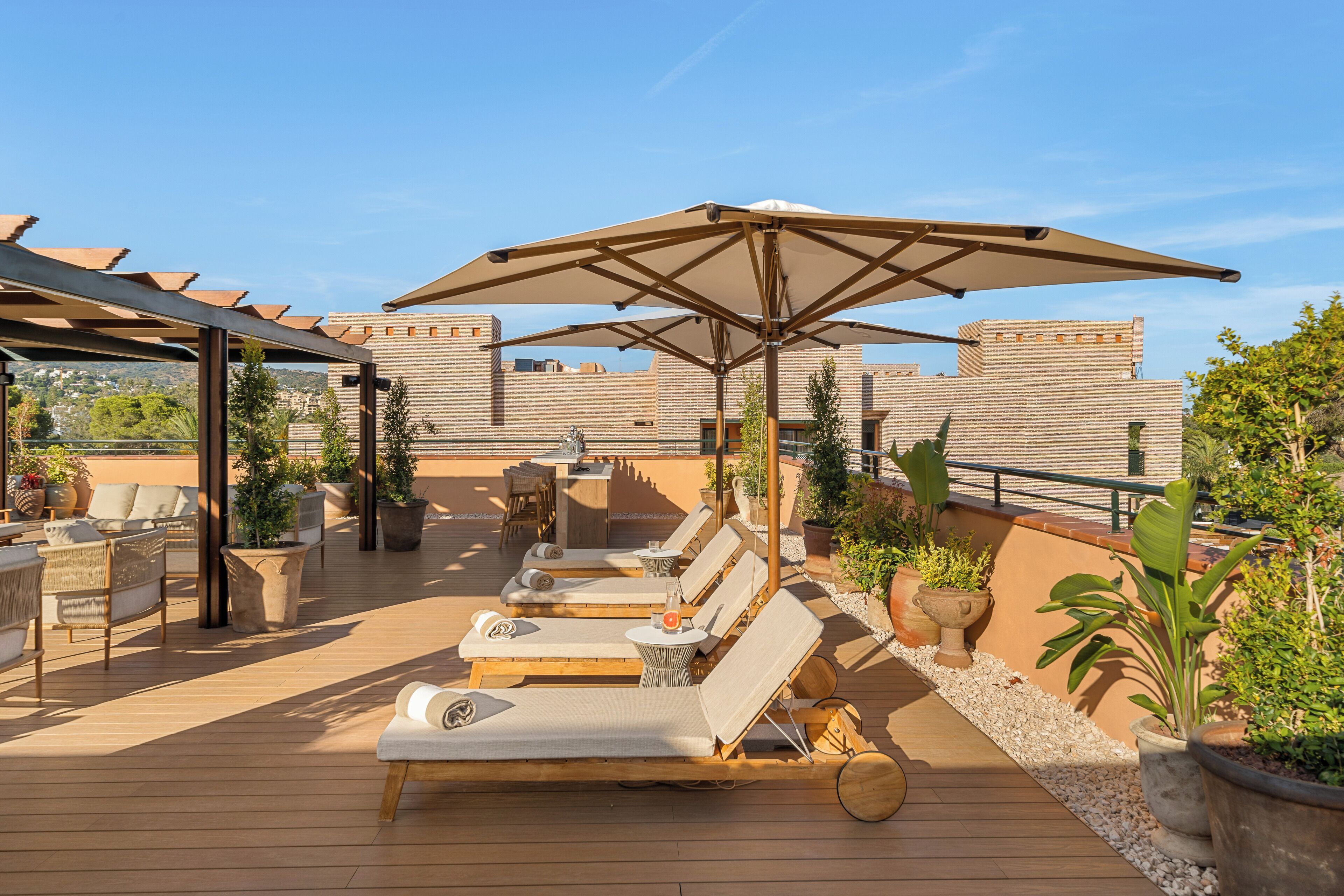 Une terrasse sur le toit, aménagée avec des chaises longues, des parasols et des plantes en pot.