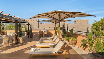 A rooftop terrace with lounge chairs, umbrellas, and potted plants.