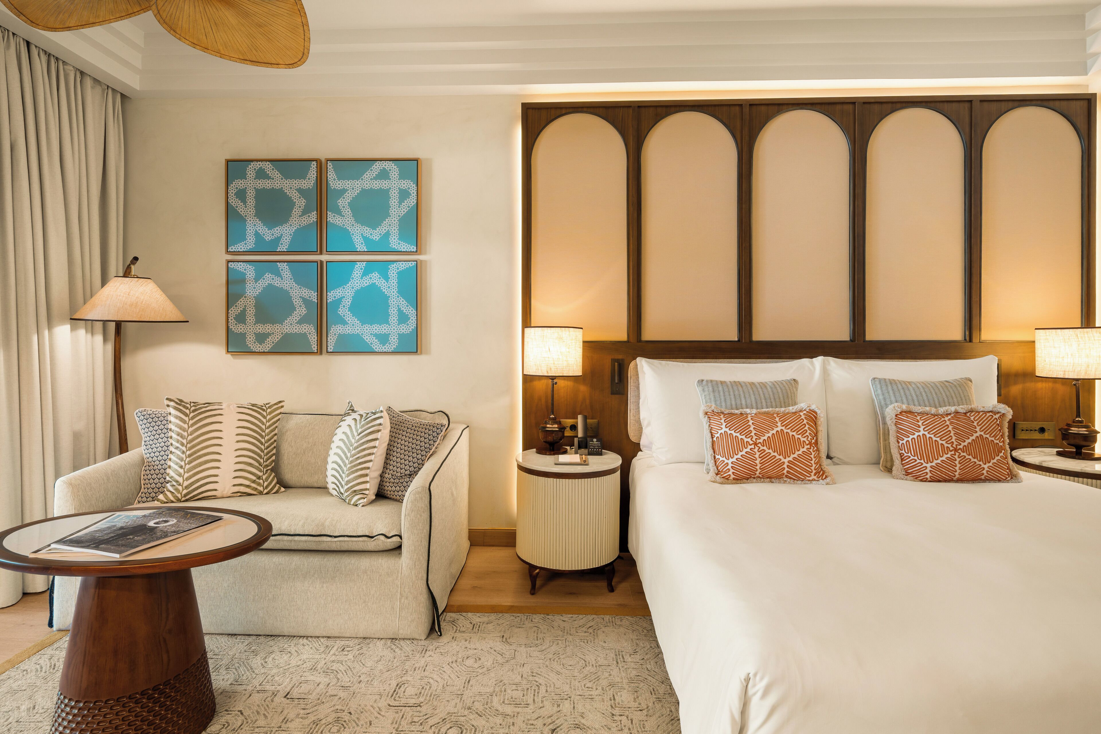 Une chambre d’hôtel avec un lit, un canapé, une table de chevet, une lampe et des œuvres d’art accrochées au mur.