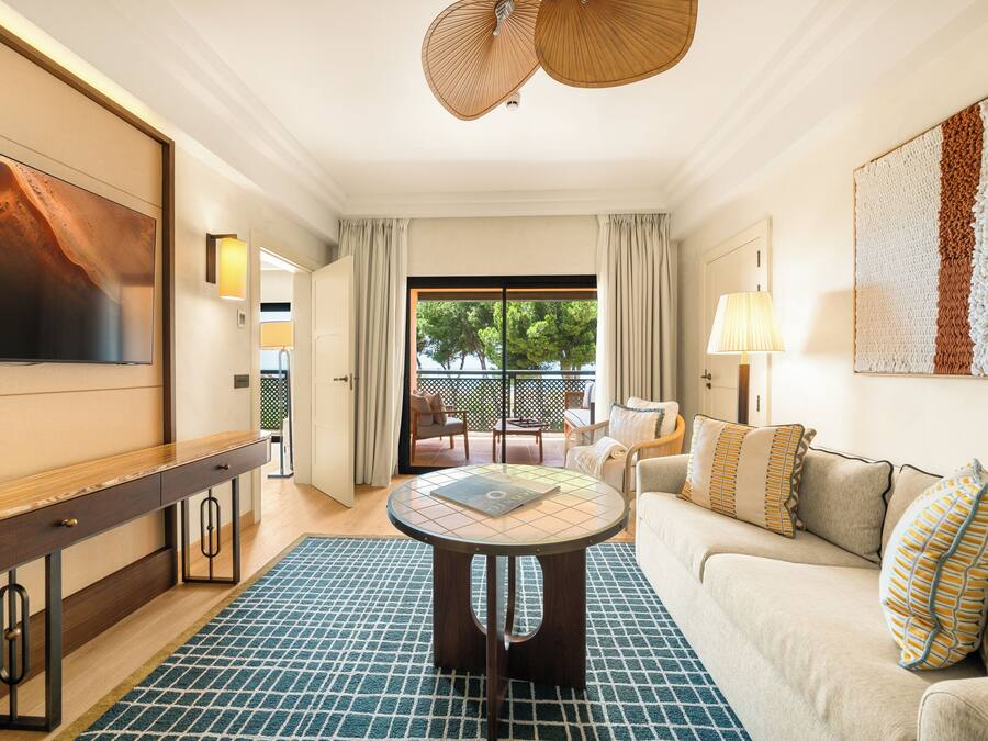 Une chambre d’hôtel dotée d’une grande télévision, d’une table ronde, d’un canapé et offrant une vue sur l’extérieur.