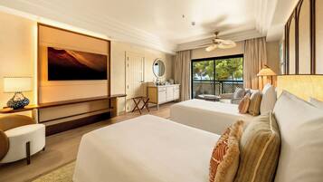 A hotel room with a large bed, a desk, a chair, a small table, a window with a view of trees, and a ceiling fan.