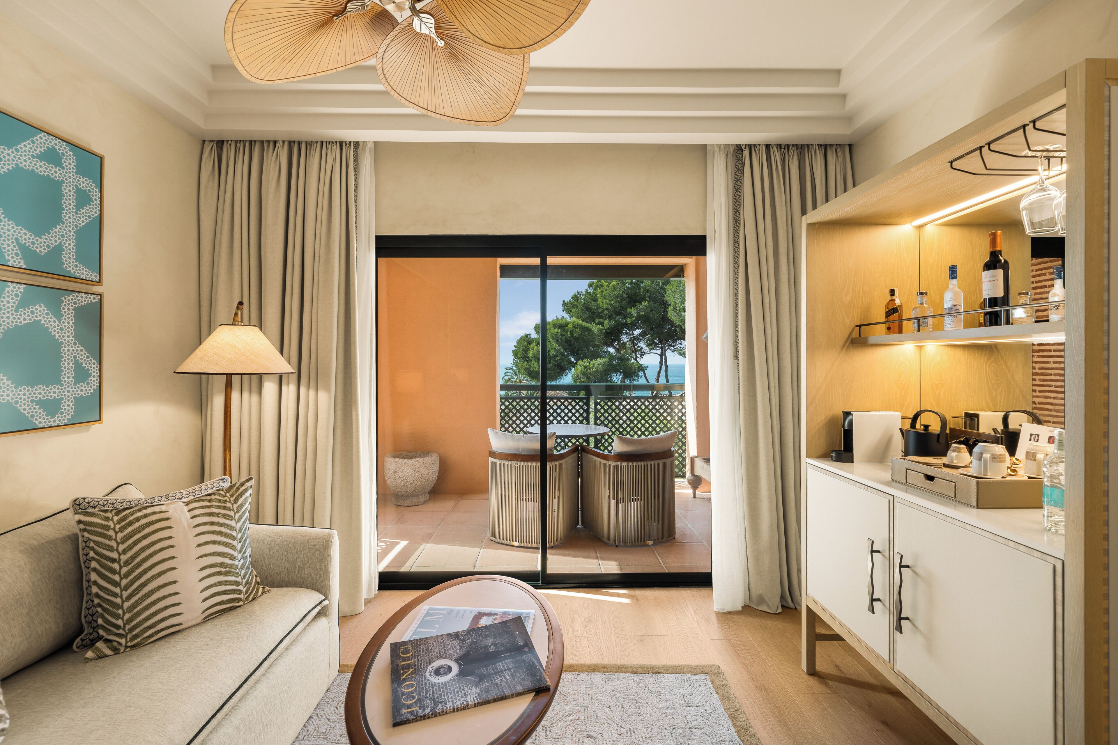 A modern living room with a sofa, a coffee table, a lamp, and a view of the outdoors through a glass door.