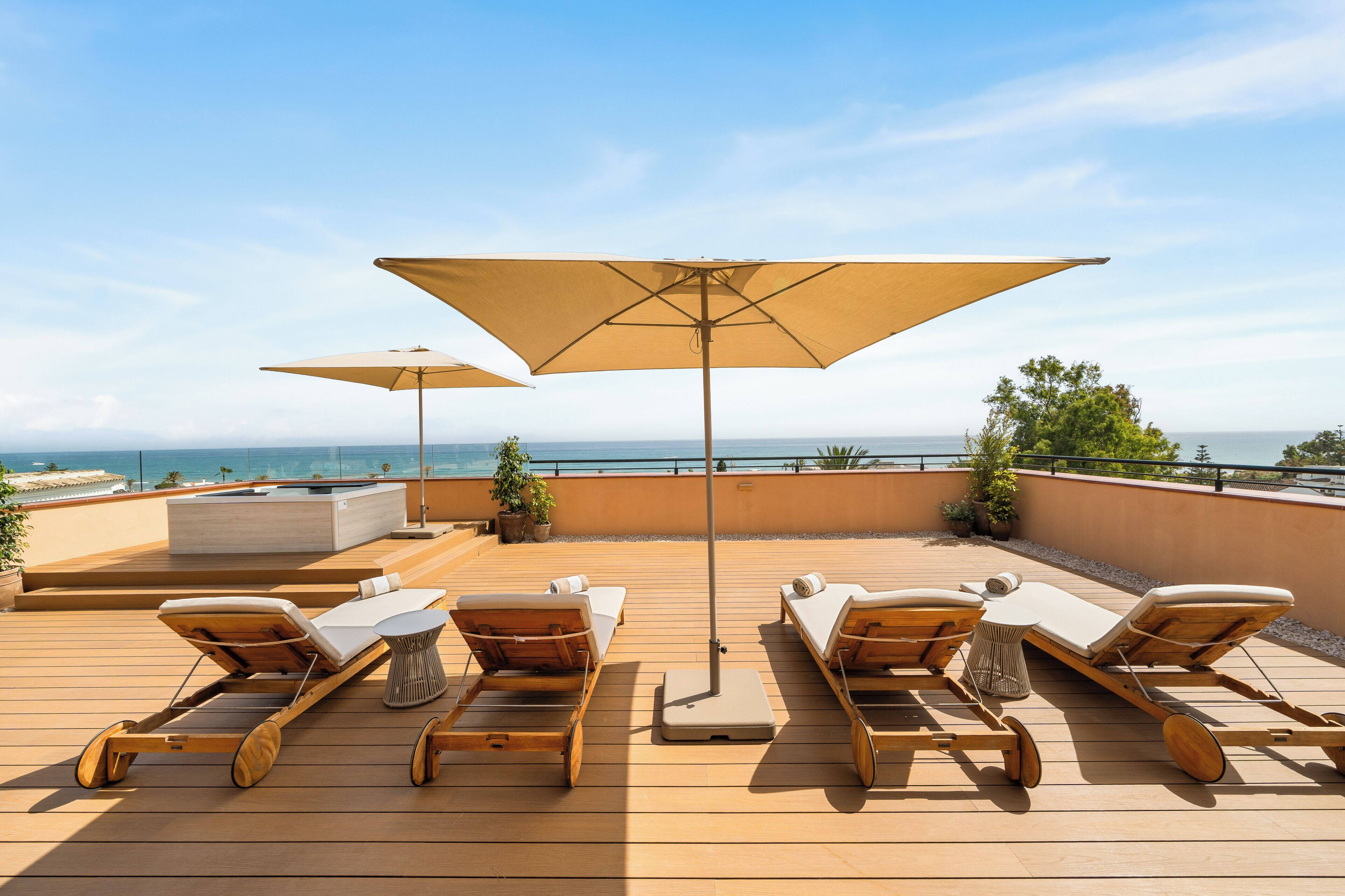 Terraza de madera con sillones de descanso y sombrillas, con vista al agua.