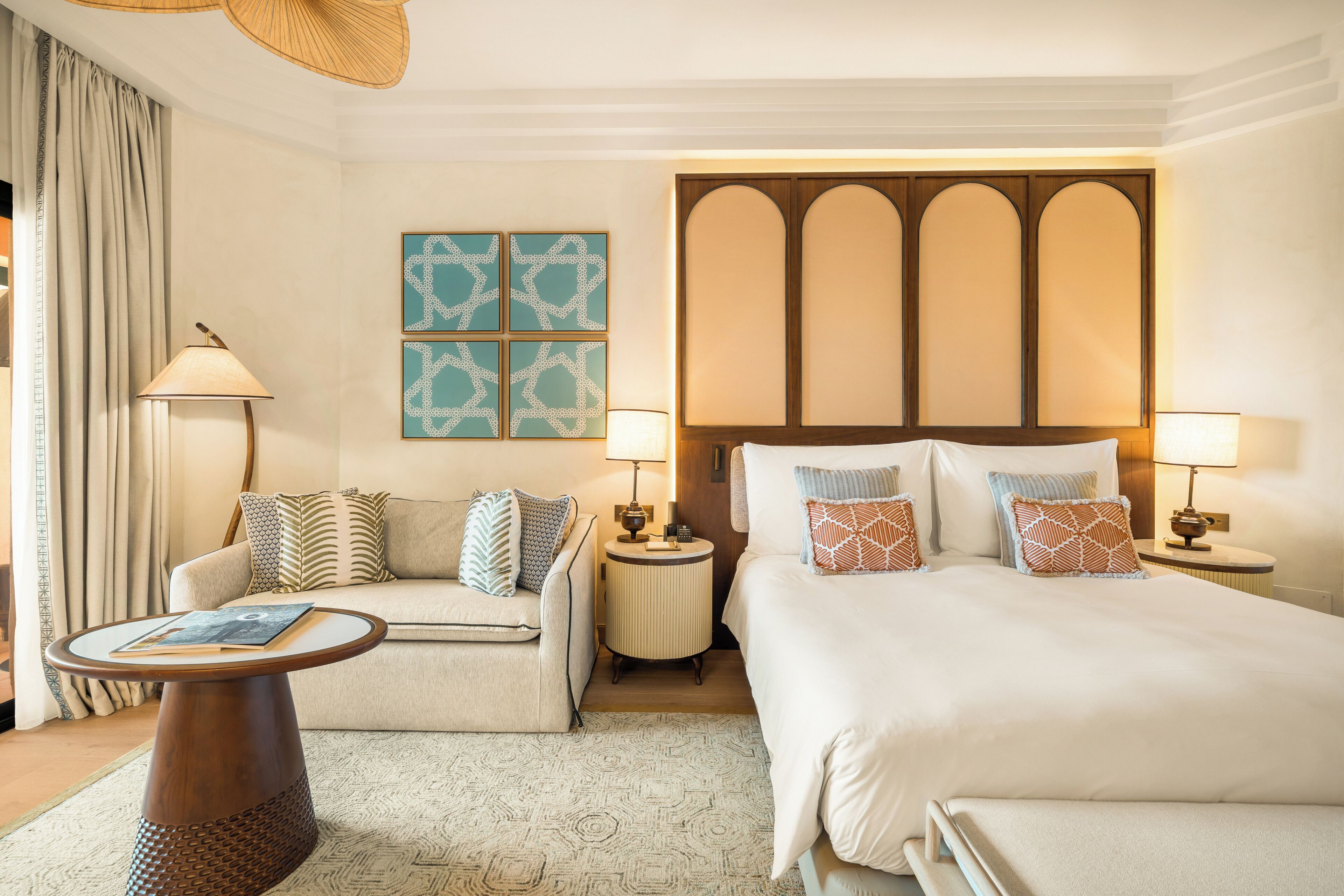 A hotel room with a bed, a sofa, a nightstand, a lamp, and a wall with artwork.